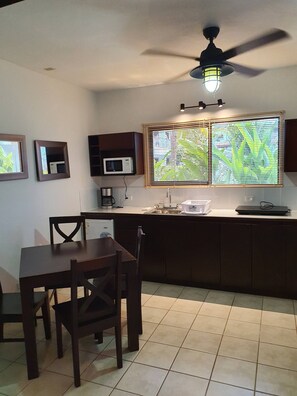 Una cocina con una mesa de comedor, sillas, un ventilador de techo, un microondas y una ventana con persianas.