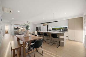 A modern kitchen with a central island, bar stools, and a dining table with chairs. - Coastal Luxury in Ocean Reef with Sunset Views (Ocean Reef)