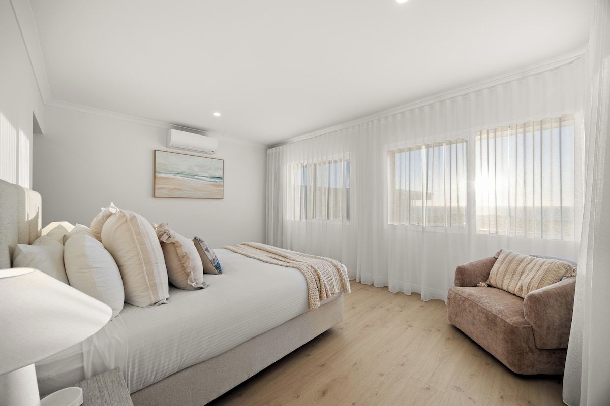 A modern bedroom with a bed, a sofa, and a window with sheer curtains.