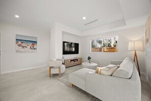 A modern living room with a sofa, a television, and artwork on the walls. - Coastal Luxury in Ocean Reef with Sunset Views (Ocean Reef)