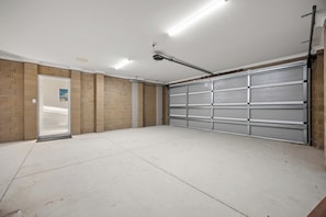 A garage with a concrete floor, a metal garage door, and a door leading to a hallway.