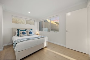 A bedroom with a bed, a nightstand, a window, and a door. - Coastal Luxury in Ocean Reef with Sunset Views (Ocean Reef)