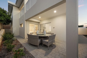 An outdoor patio with a round table and chairs, a brick pathway, and a building with a glass door.