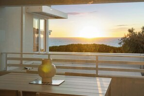 A balcony with a view of the sunset over the sea, a wooden table, and a vase. - Coastal Luxury in Ocean Reef with Sunset Views (Ocean Reef)