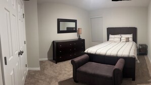 A bedroom with a bed, a dresser, a chair, a nightstand, and a window with blinds. - Vrbo Property (Haines City)