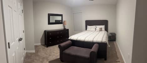 A bedroom with a bed, a dresser, a chair, a nightstand, and a window with blinds.