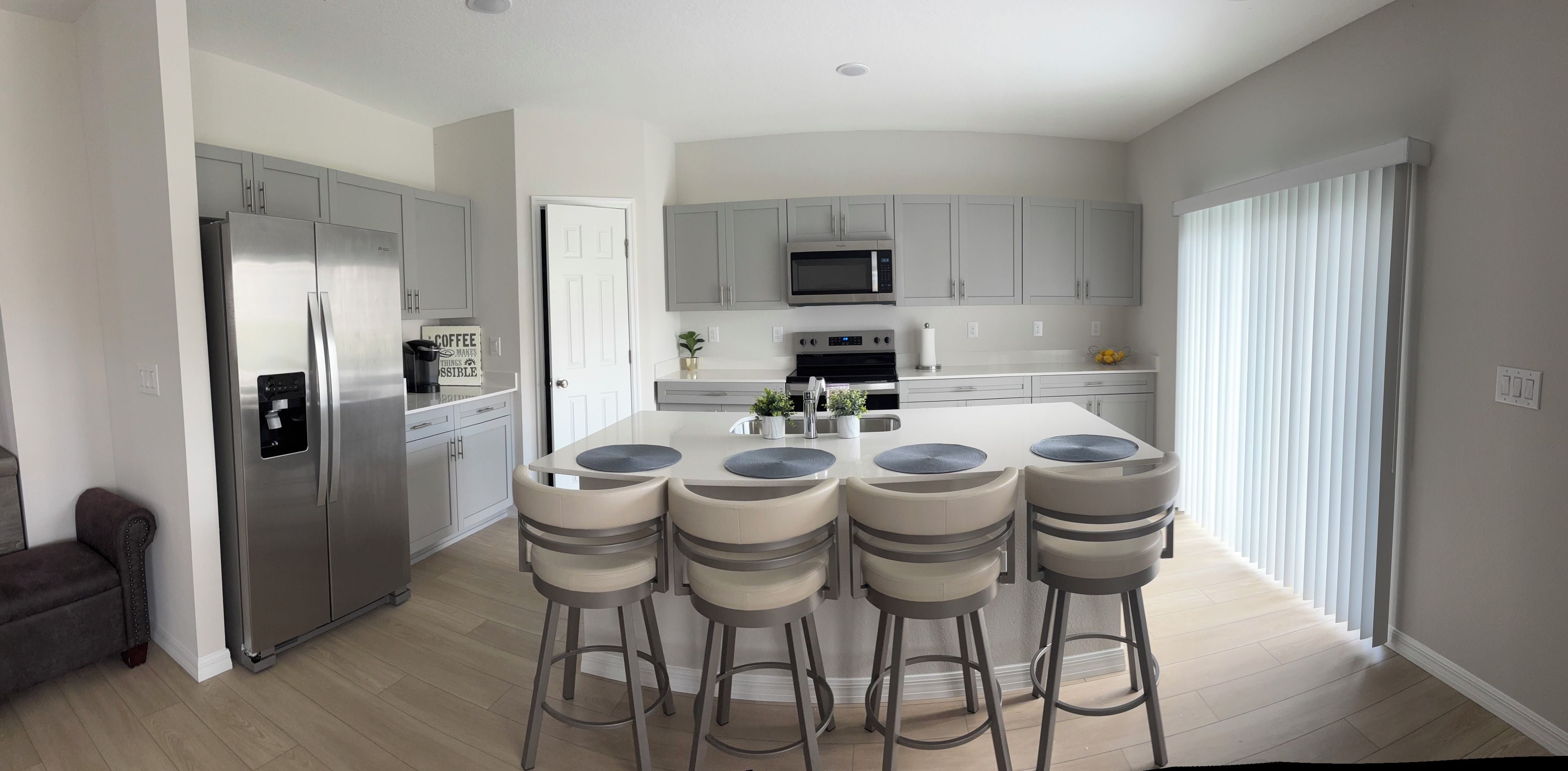 Una cocina moderna con una isla central, taburetes de bar, electrodomésticos de acero inoxidable y armarios de colores claros.