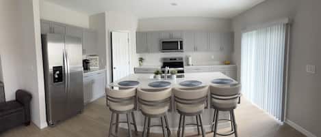 A modern kitchen with a central island, bar stools, stainless steel appliances, and light-colored cabinetry.