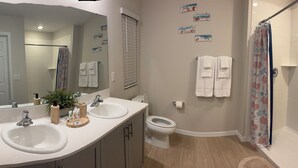 A bathroom with two sinks, a toilet, a shower with a floral curtain, and a mirror with a plant. - Vrbo Property (Haines City)