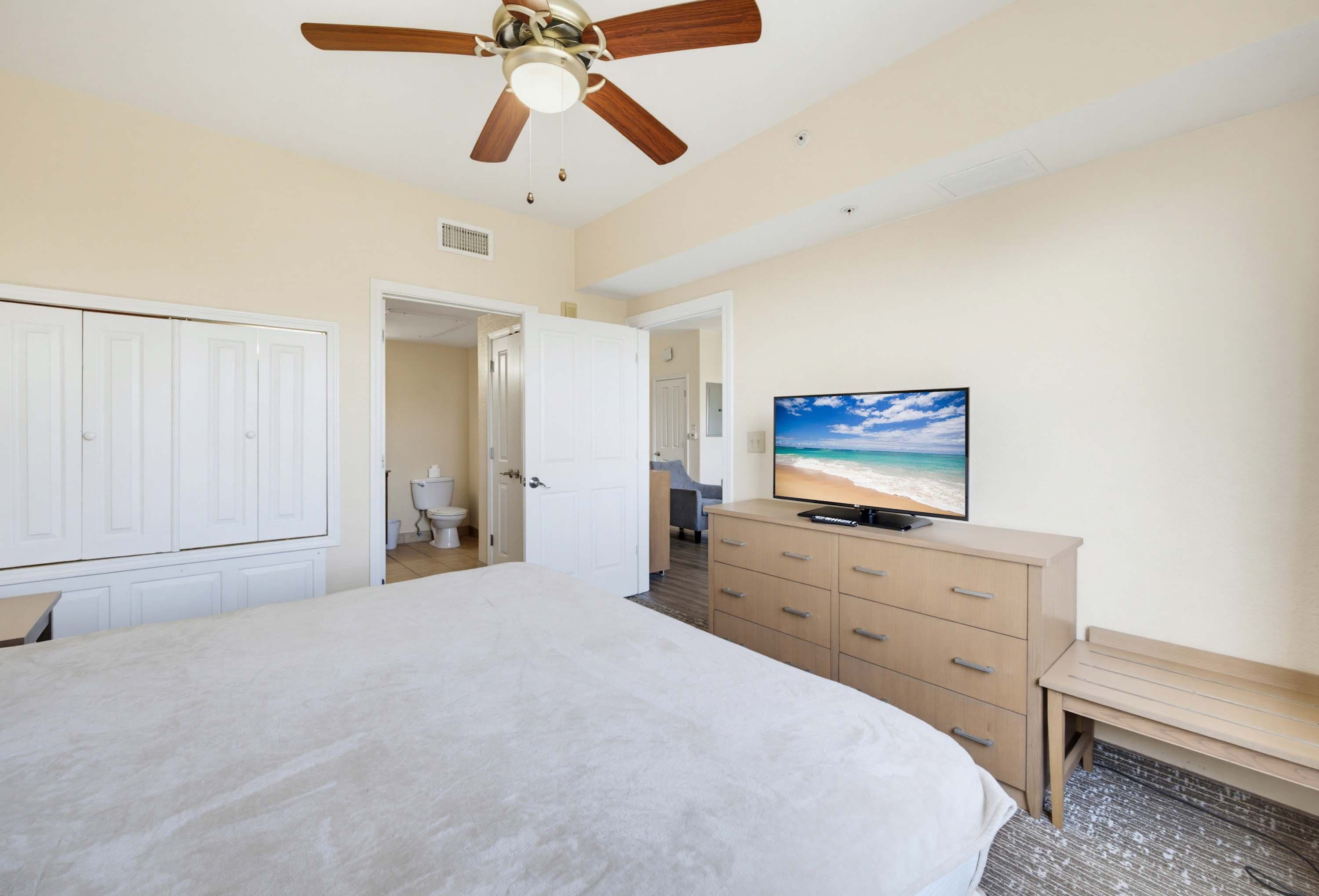 Un dormitorio con cama, televisor, ventilador de techo y vista a la playa.