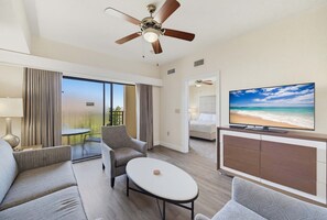 A hotel room with a large TV, a ceiling fan, a sofa, a coffee table, and a view of the beach. - Modern 2B Resort Condo Just 8 Minutes to Disney (Orlando)
