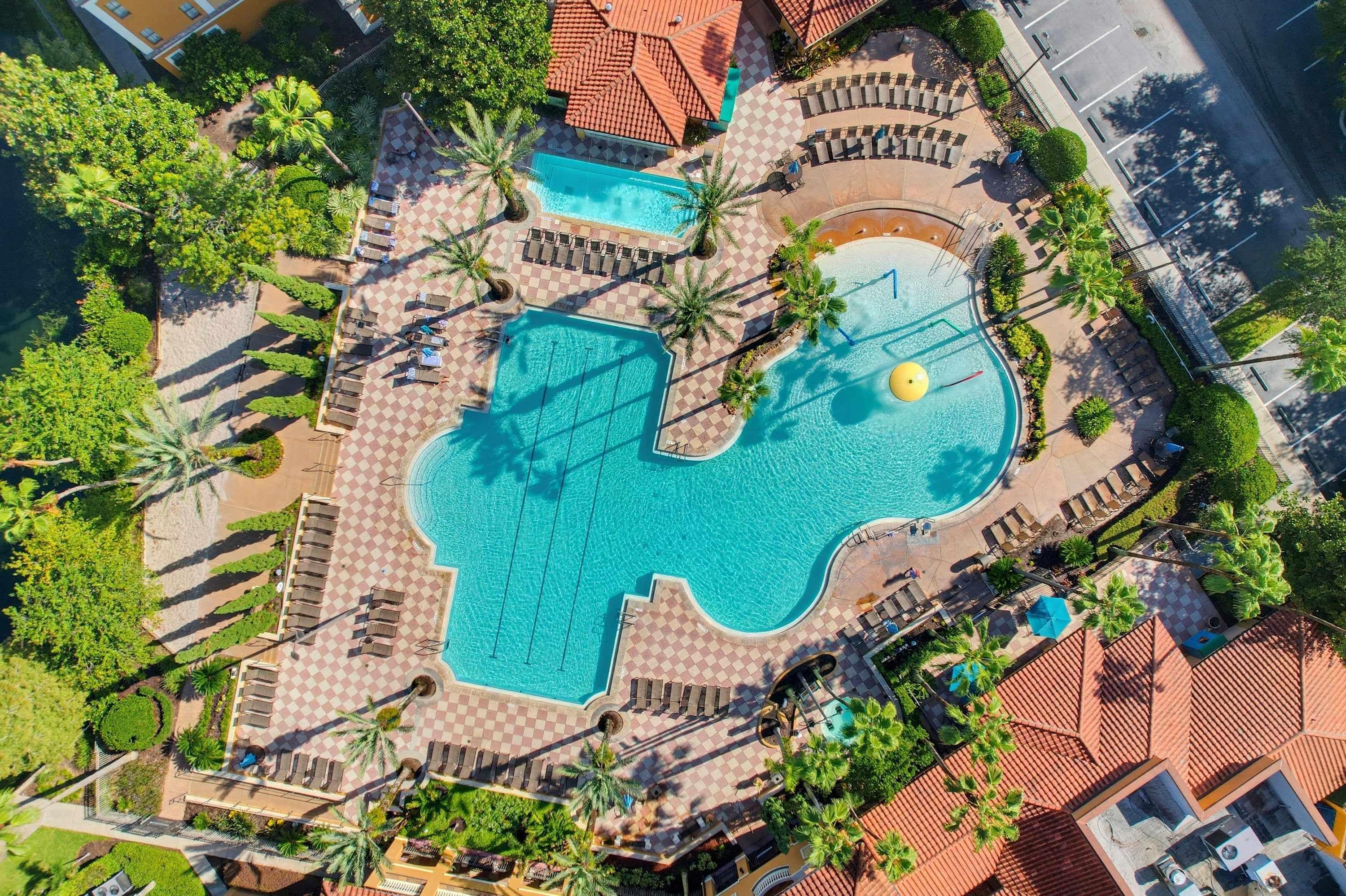 Vista aérea de um resort com uma piscina central grande, várias piscinas menores e espreguiçadeiras dispostas ao redor das piscinas.