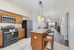 A modern kitchen with stainless steel appliances, wooden cabinets, and a central island with bar stools. - Modern 2B Resort Condo Just 8 Minutes to Disney (Orlando)