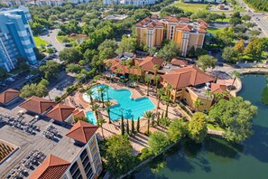 A resort with a central swimming pool, multiple buildings with red-tiled roofs, and lush greenery surrounding the area. - Modern 2B Resort Condo Just 8 Minutes to Disney (Orlando)