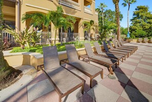 A row of sun loungers with a poolside view, a building with balconies, and tropical landscaping. - Modern 2B Resort Condo Just 8 Minutes to Disney (Orlando)