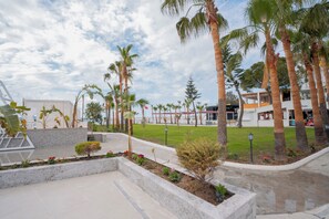 A landscaped outdoor area with palm trees, a paved walkway, and a building with a sign that reads 'Center.' - Mira Meridia Beach Resort Hotel (Alanya)