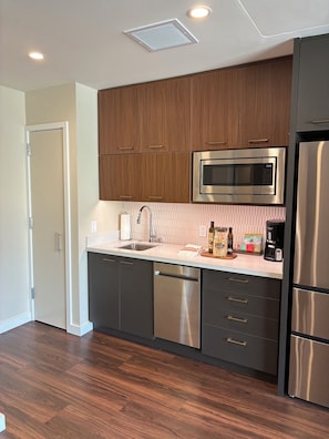 A modern kitchen with wooden cabinets, stainless steel appliances, a microwave, and a dishwasher. - Newly Built & Fully Equipped | Enjoy a Waikiki Stay for Up to 6 People (Honolulu)