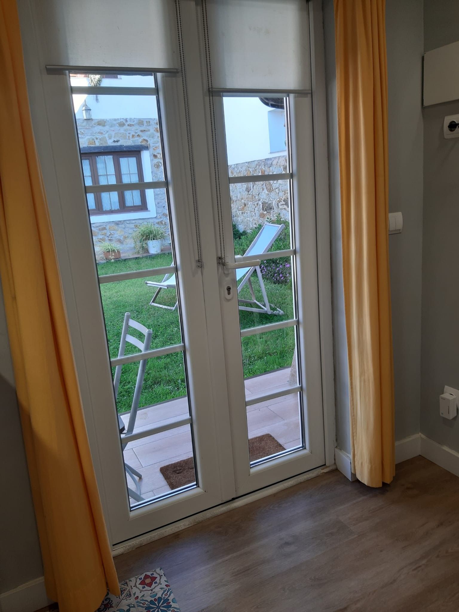 Una habitación con puerta de vidrio corrediza que da a un espacio exterior con césped y un edificio de piedra al fondo.