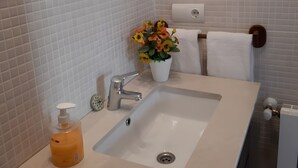 A bathroom with a white sink, a mirror, a towel rack, and a potted plant with flowers. - Holiday Home 'Estudio Minimalista En Galizano' with Private Terrace, Private Garden and Wi-Fi (Cantabria)