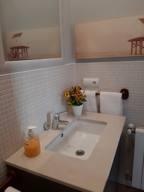 Une salle de bain avec un lavabo blanc, un miroir, un porte-serviettes et une plante en pot avec des fleurs.