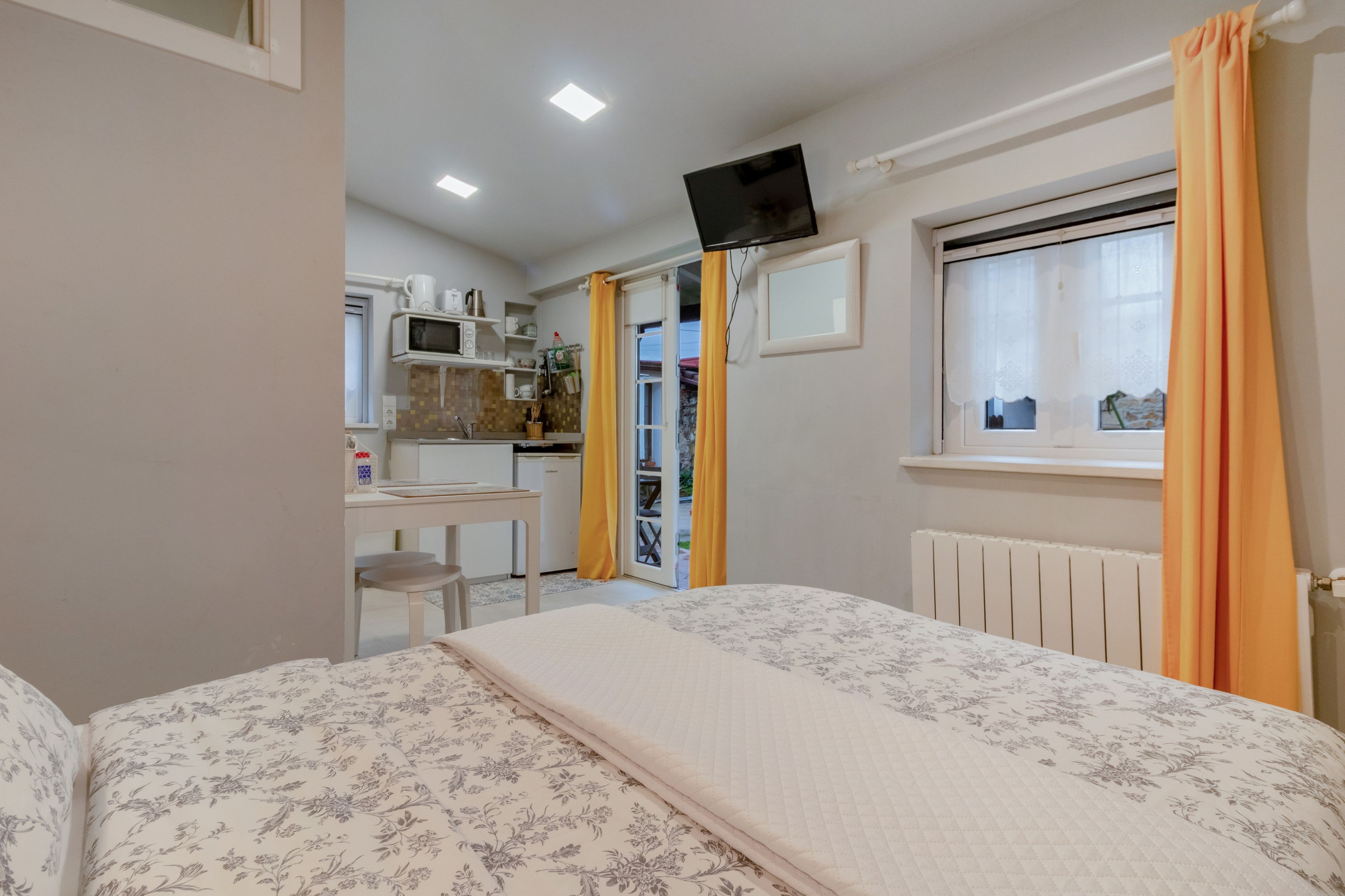 Un dormitorio con cama, televisor montado en la pared, ventana con cortinas y vistas al exterior.