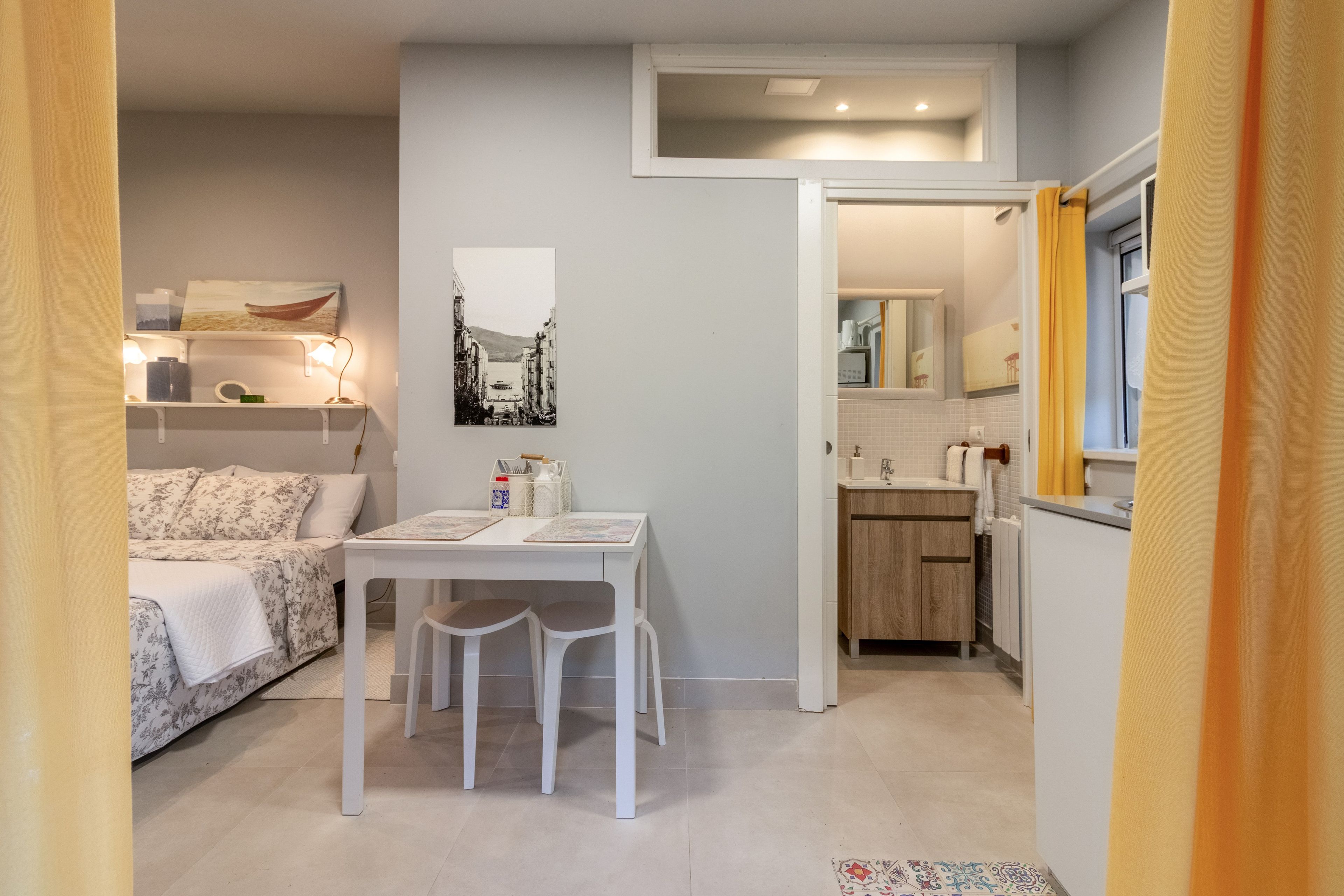 Une pièce de taille modeste comprenant un lit, une table à manger avec des chaises, un coin cuisine et une salle de bain.