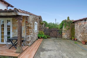 A stone building with a wooden deck and a table with chairs. - Holiday Home 'Estudio Minimalista En Galizano' with Private Terrace, Private Garden and Wi-Fi (Cantabria)