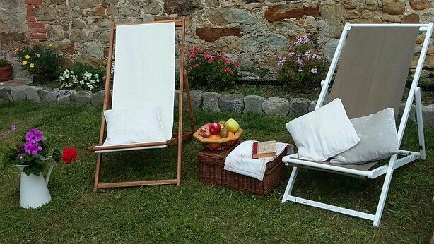 Two outdoor seating areas with white cushions, a picnic basket with fruits, and a white vase with flowers. - Holiday Home 'Estudio Minimalista En Galizano' with Private Terrace, Private Garden and Wi-Fi (Cantabria)