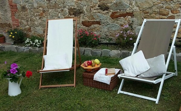 Deux espaces de détente en plein air avec des coussins blancs, un panier de pique-nique rempli de fruits et un vase blanc orné de fleurs.