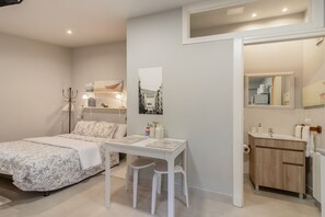 A bedroom with a bed, a desk, and a chair. There is a bathroom with a sink and a mirror.