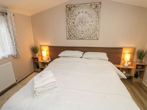 A neatly made bed with white linens, two bedside tables with lamps, a radiator, and a decorative wall piece. - Serenity Thorness Bay (Cowes)