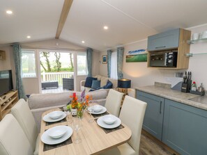 A modern kitchen with a dining area, a TV, and a view of the outdoors. - Serenity Thorness Bay (Cowes)