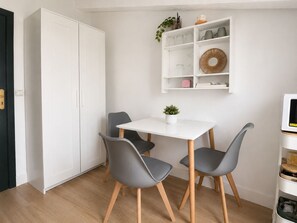 Ein kleiner Essbereich mit einem weißen Tisch und zwei grauen Stühlen, einem weißen Schrank und einem Regal mit Dekoration.