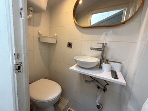 Ein kleines, kompaktes Badezimmer mit Toilette, Waschbecken mit Spiegel darüber und einem Handtuchspender.