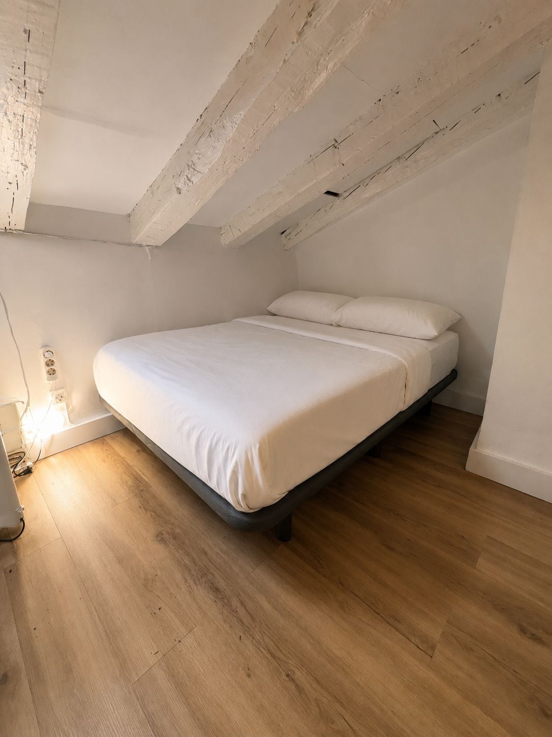 A single bed in a room with wooden flooring and white walls.