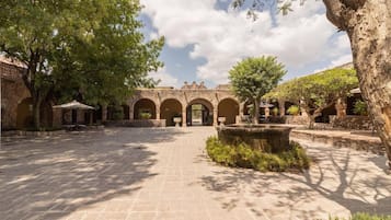 Un patio con suelo de piedra, arcos y árboles que dan sombra.