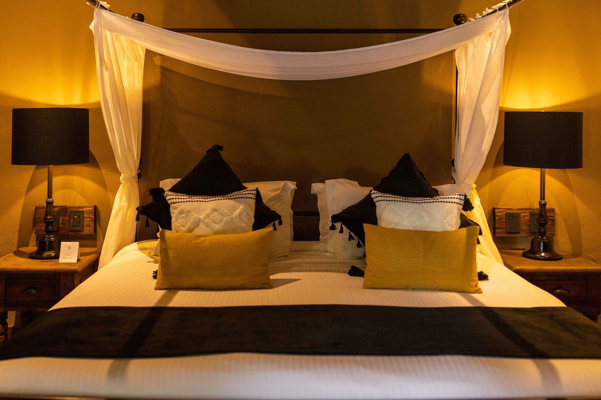 Una cama con dosel, dos mesitas de noche con lámparas y almohadillas.