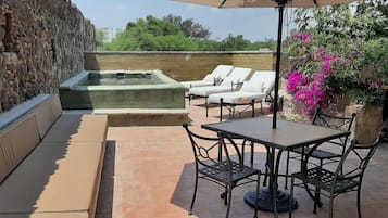 Un patio con muro de piedra, jacuzzi, sillas de descanso y una mesa con sillas.
