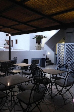 An outdoor patio area with tables and chairs, a potted plant, and a staircase leading to an upper level. - Le Sette Vele B&B (Santa Marina Salina)