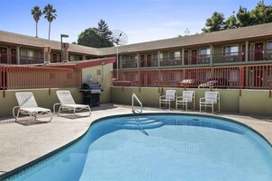 A swimming pool with lounge chairs, a barbecue grill, and a motel building with balconies.