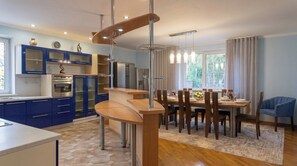 Una cucina moderna con mobili azzurri, un'area pranzo con tavolo e sedie in legno, e vista sul verde circostante.
