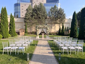 An outdoor wedding venue with a clear pathway leading to an arch decorated with flowers, surrounded by rows of white chairs.