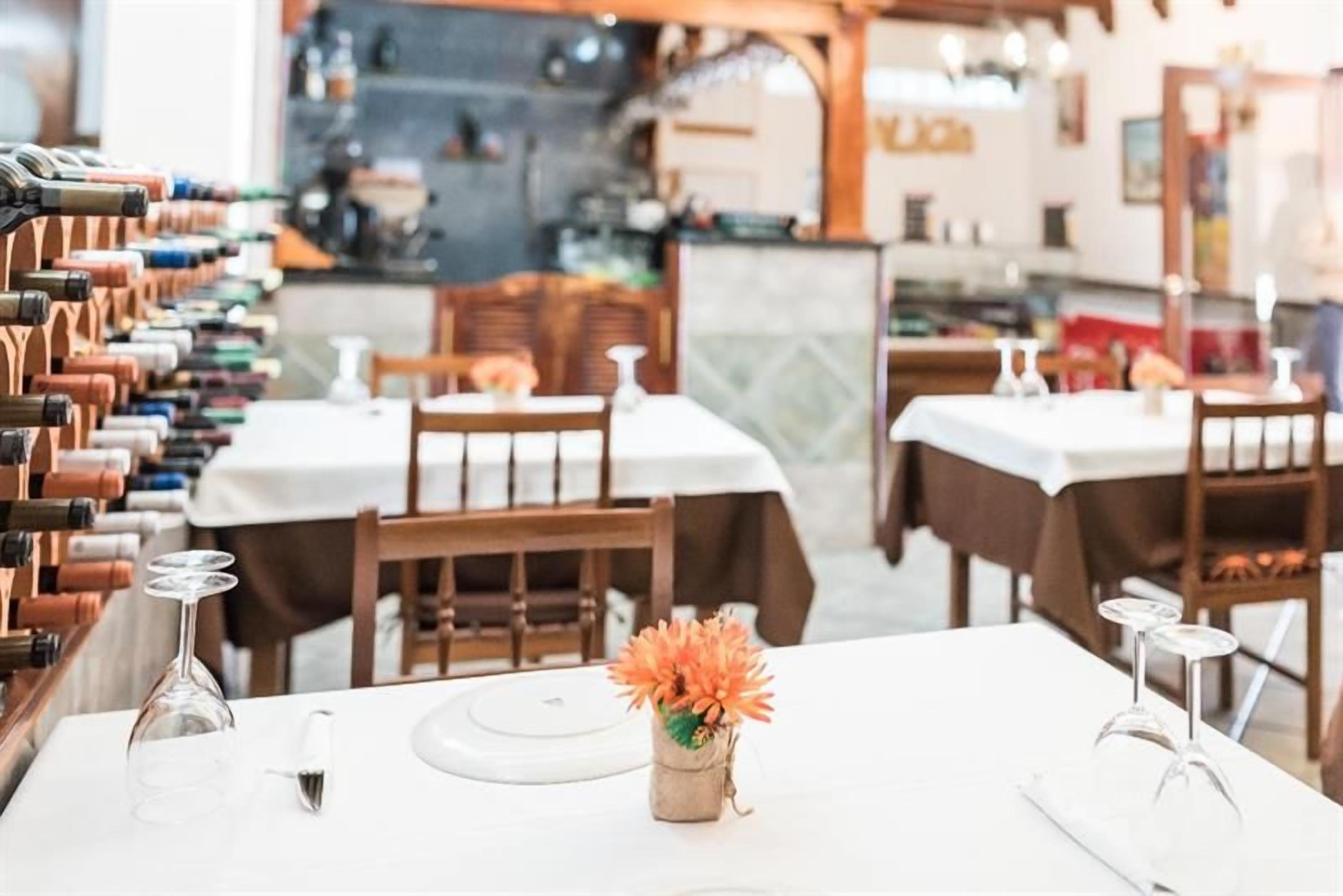 Interior de un restaurante con mesas dispuestas para comer, una bodega de vinos y un centro de mesa con flores.
