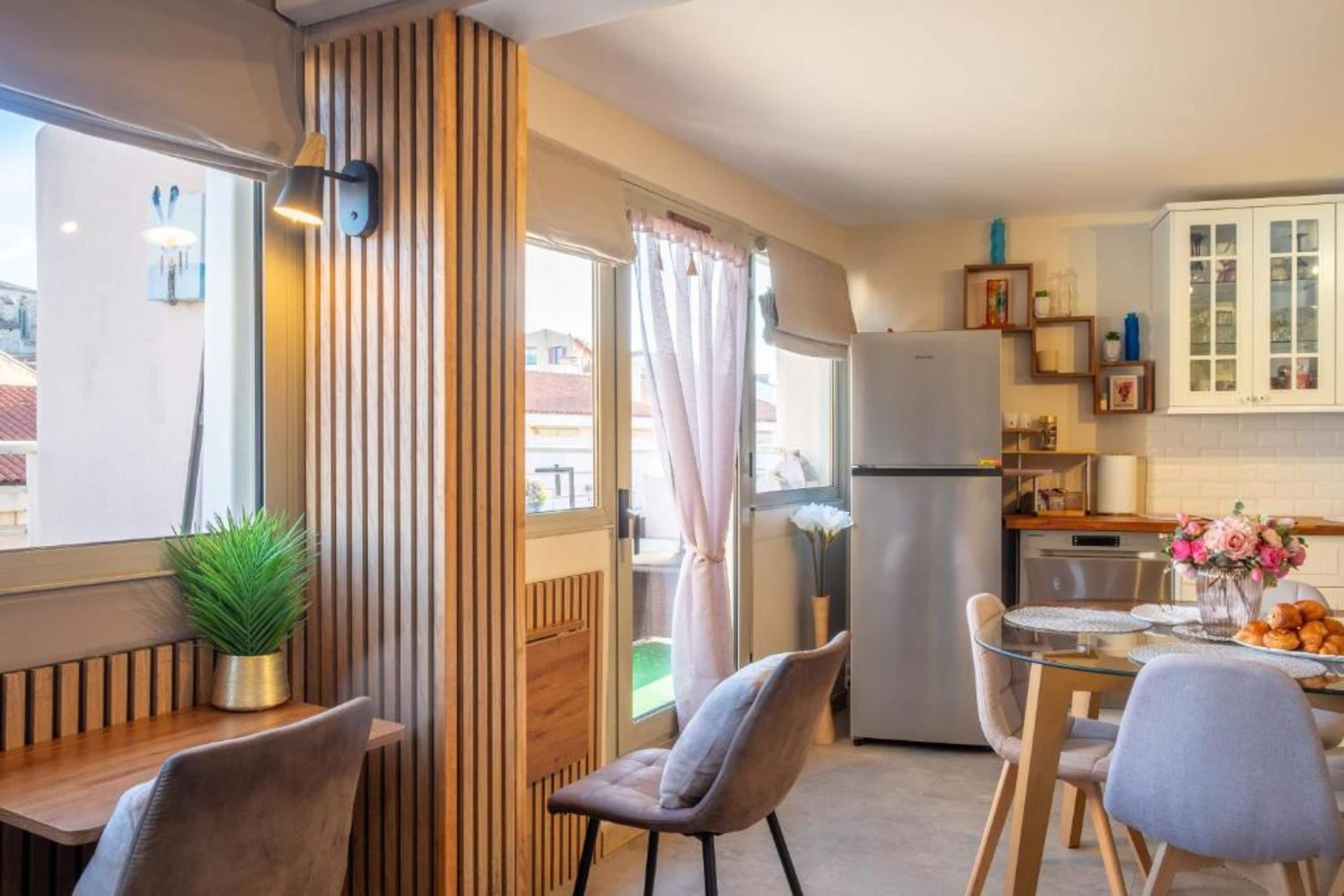 Una cocina compacta con refrigerador, una mesa de comedor con sillas y una ventana con cortinas.