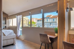 A modern apartment with a balcony, a sofa, a dining table, and a view of the cityscape.