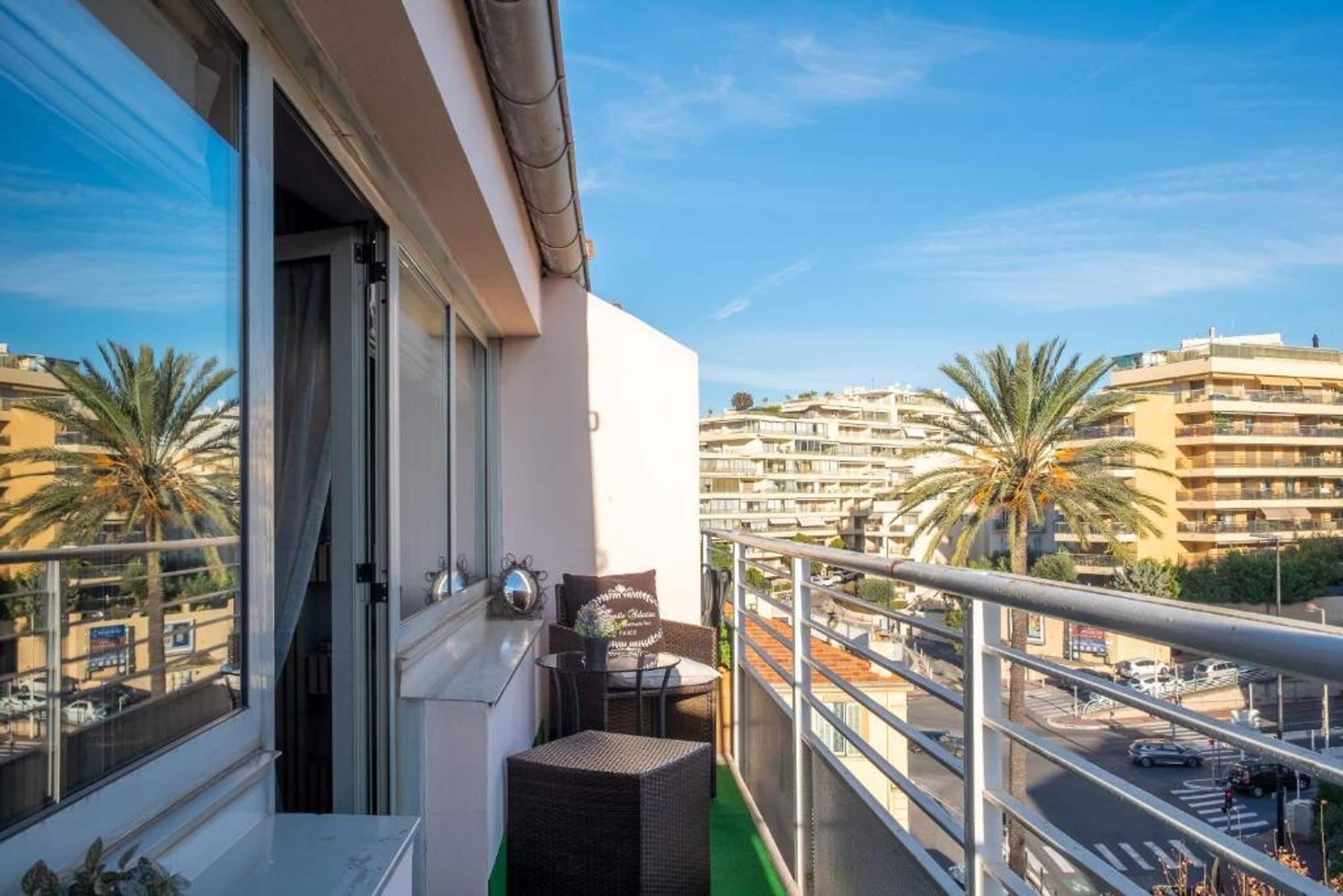 Un balcon offrant une vue sur le paysage urbain, avec des palmiers et des immeubles à plusieurs étages.