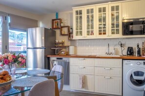 A modern kitchen with white cabinetry, stainless steel appliances, and a glass dining table with a vase of flowers. - Lovely Modern top Floor Apartment in Central Cannes Just a Short Walk From Beaches and the Palais - 2399 (Cannes)