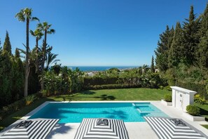 A swimming pool with a view of the ocean, surrounded by palm trees and a well-maintained lawn. - Villa In Sierra Blanca - 2398 (Marbella)