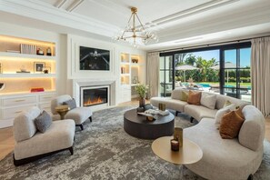 A modern living room with a fireplace, a large sofa set, and a view of a pool. - Villa In Sierra Blanca - 2398 (Marbella)