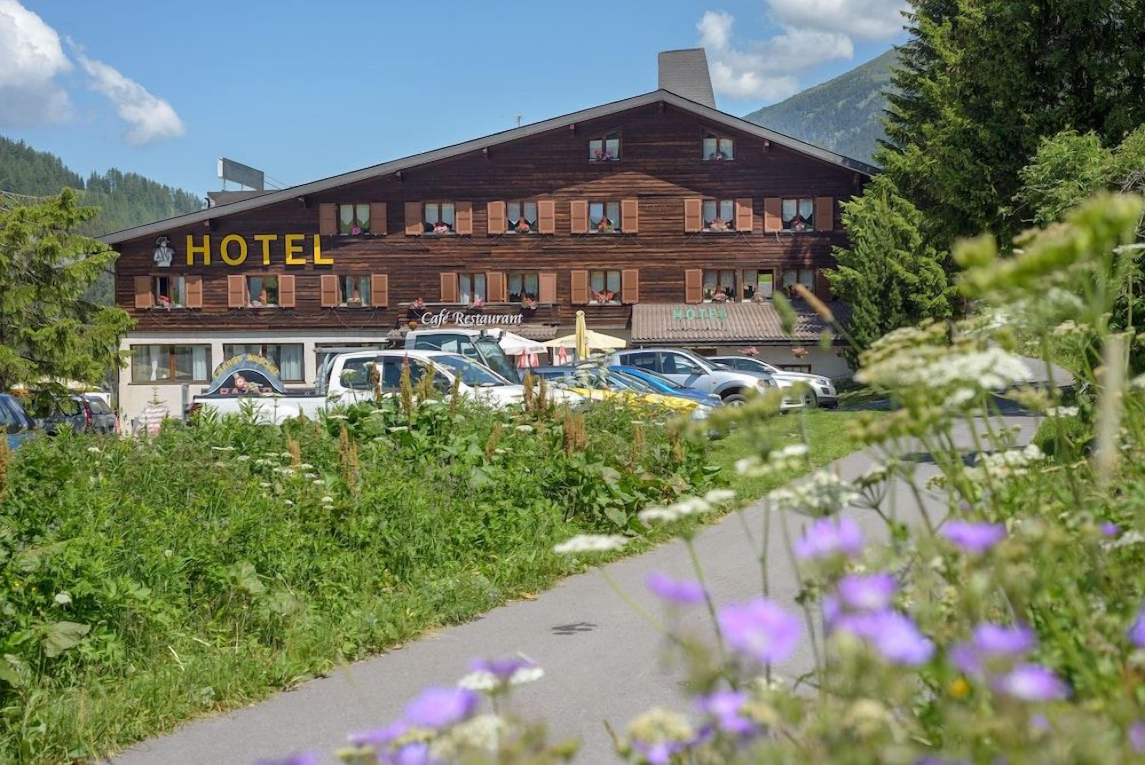 Ein Hotel mit Holzfassade, ein Café-Restaurant und ein Parkplatz mit Autos.